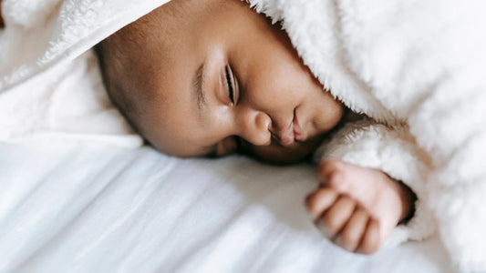 Newborn baby sleeping peacefully under a soft white blanket, promoting better baby sleep.