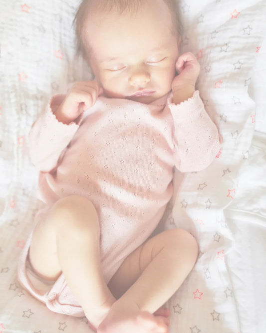 Sleeping newborn baby in pink onesie on star-patterned soft blanket