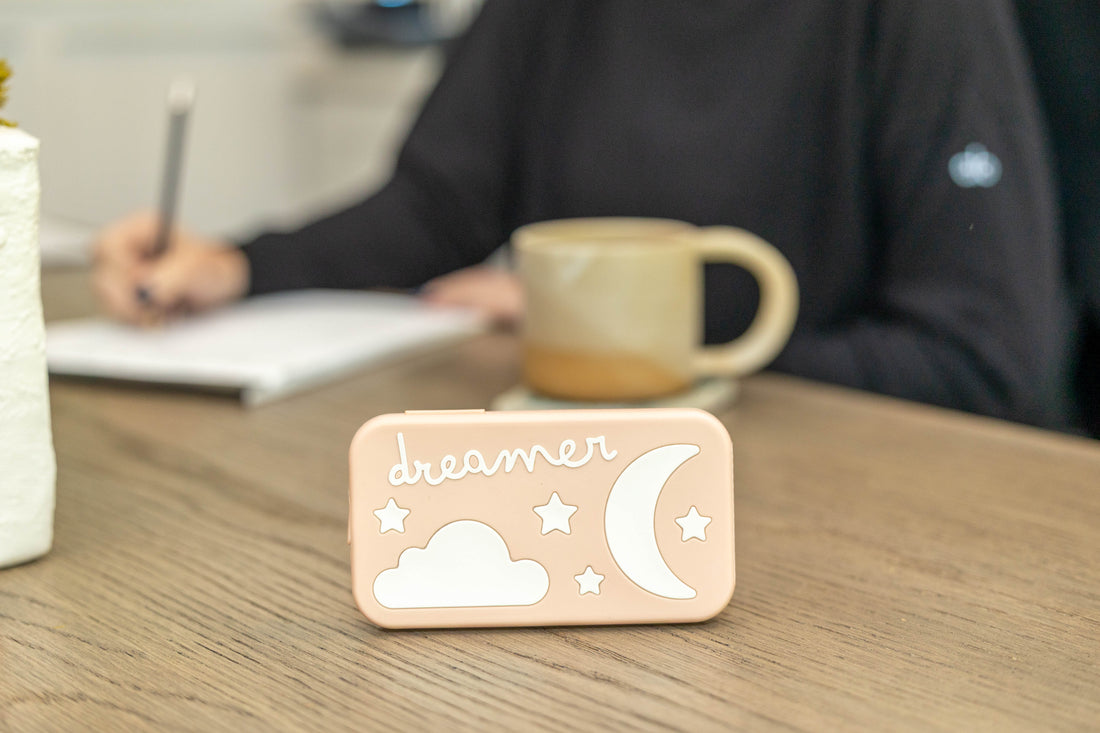 Portable baby sound machine with cloud and moon design on wooden table, coffee mug in background
