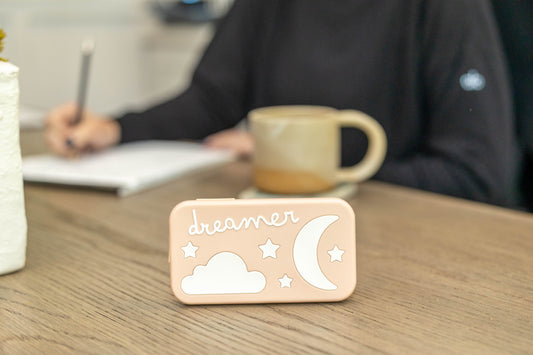 Portable baby sound machine with cloud and moon design on wooden table, coffee mug in background