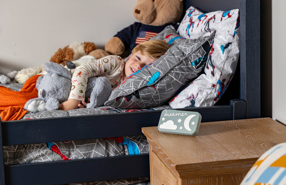 Child sleeping peacefully beside the Dreamer™ baby sound machine on a nightstand