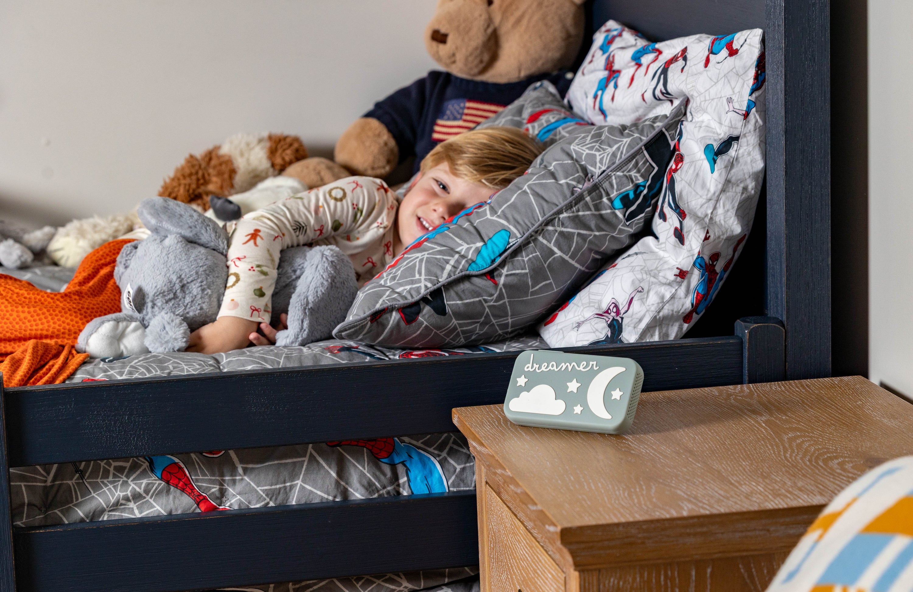Child in bed with teddy bears and pillows, next to a nightlight on a wooden nightstand.