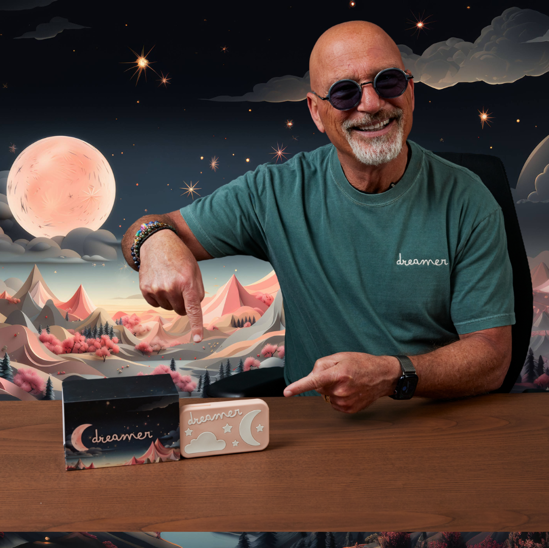 Howie mandel pointing at a dreamer device with a scenic mountain backdrop