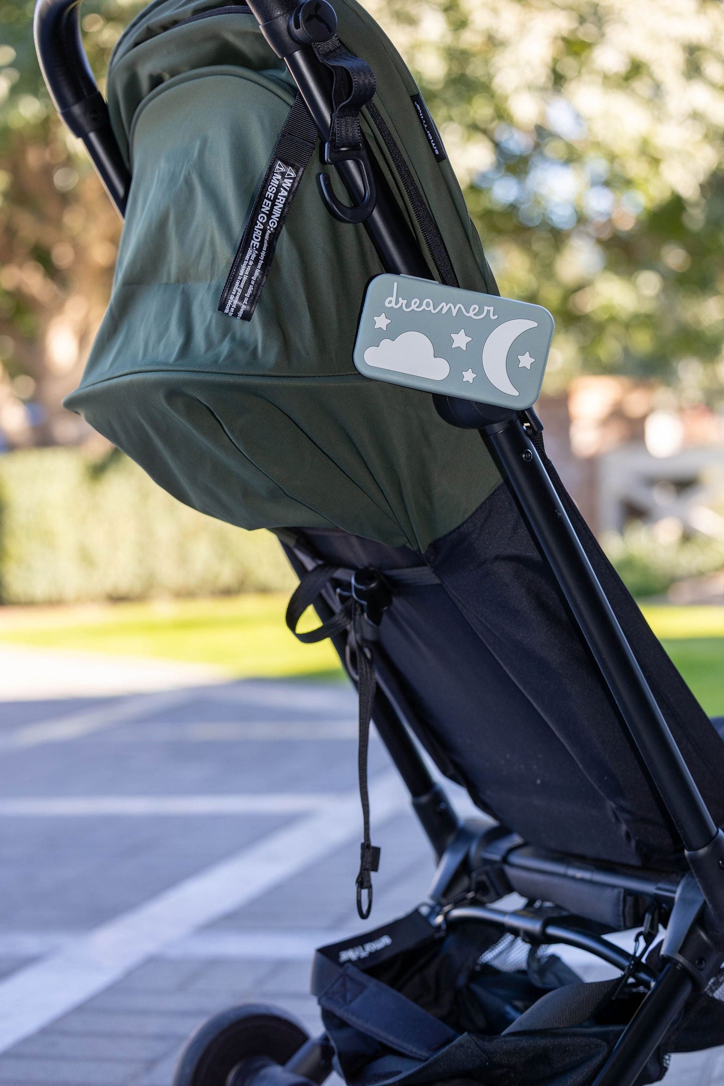 Sage green Dreamer™ baby sound machine from the Duo bundle attached to a stroller frame outdoors