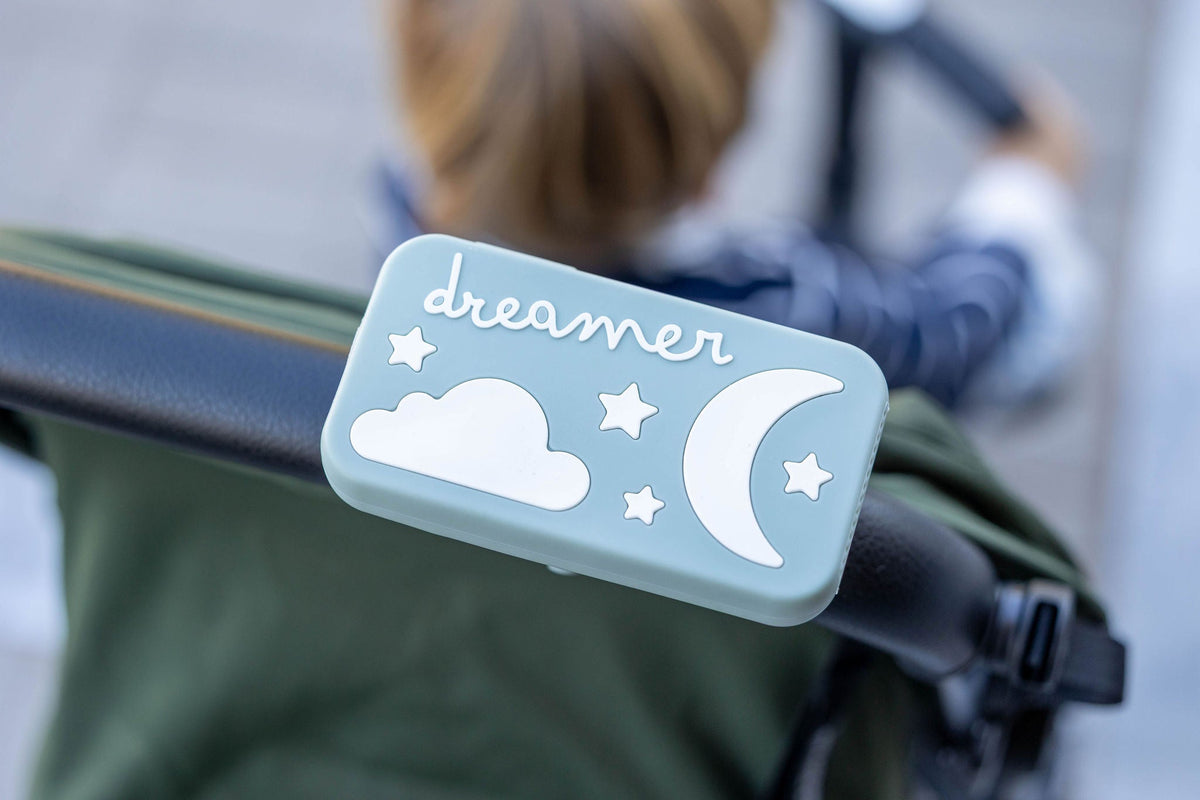 Dreamer™ baby sound machine in sage green clipped to a stroller handle with magnetic strap
