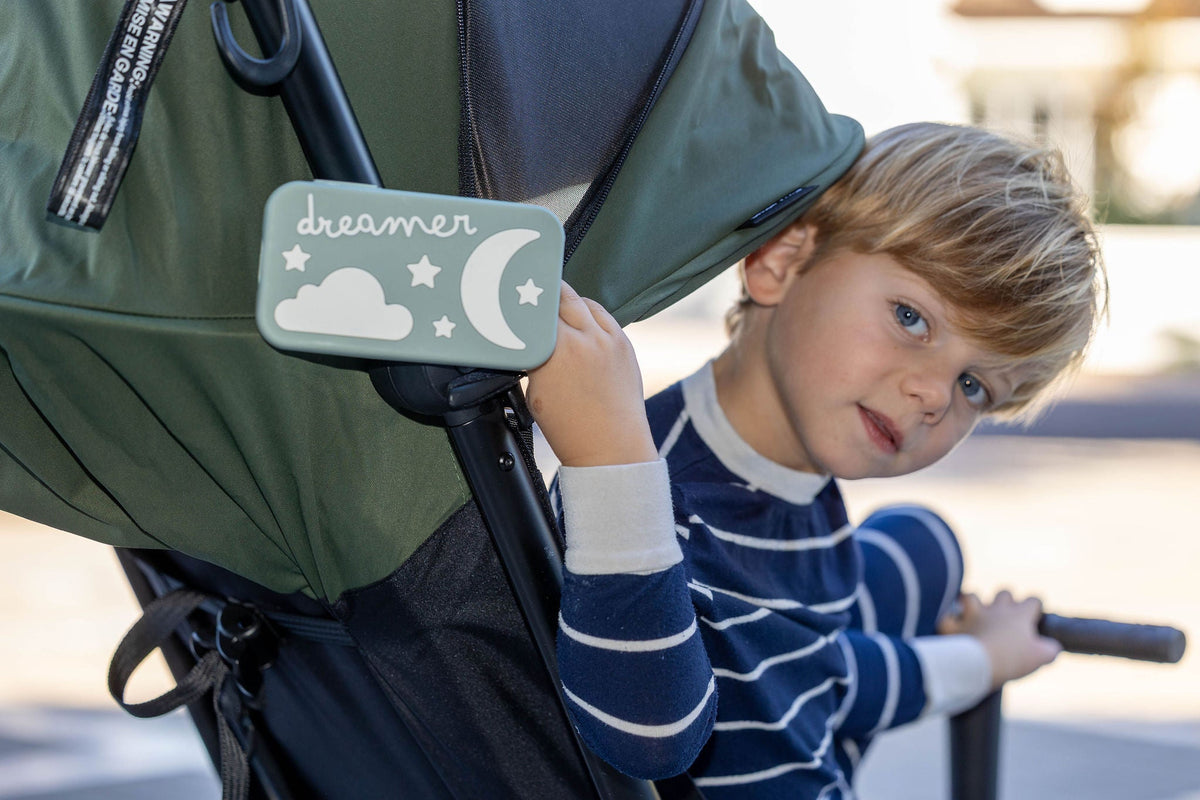 Young child in a stroller holding the Dreamer™ baby sound machine in sage green