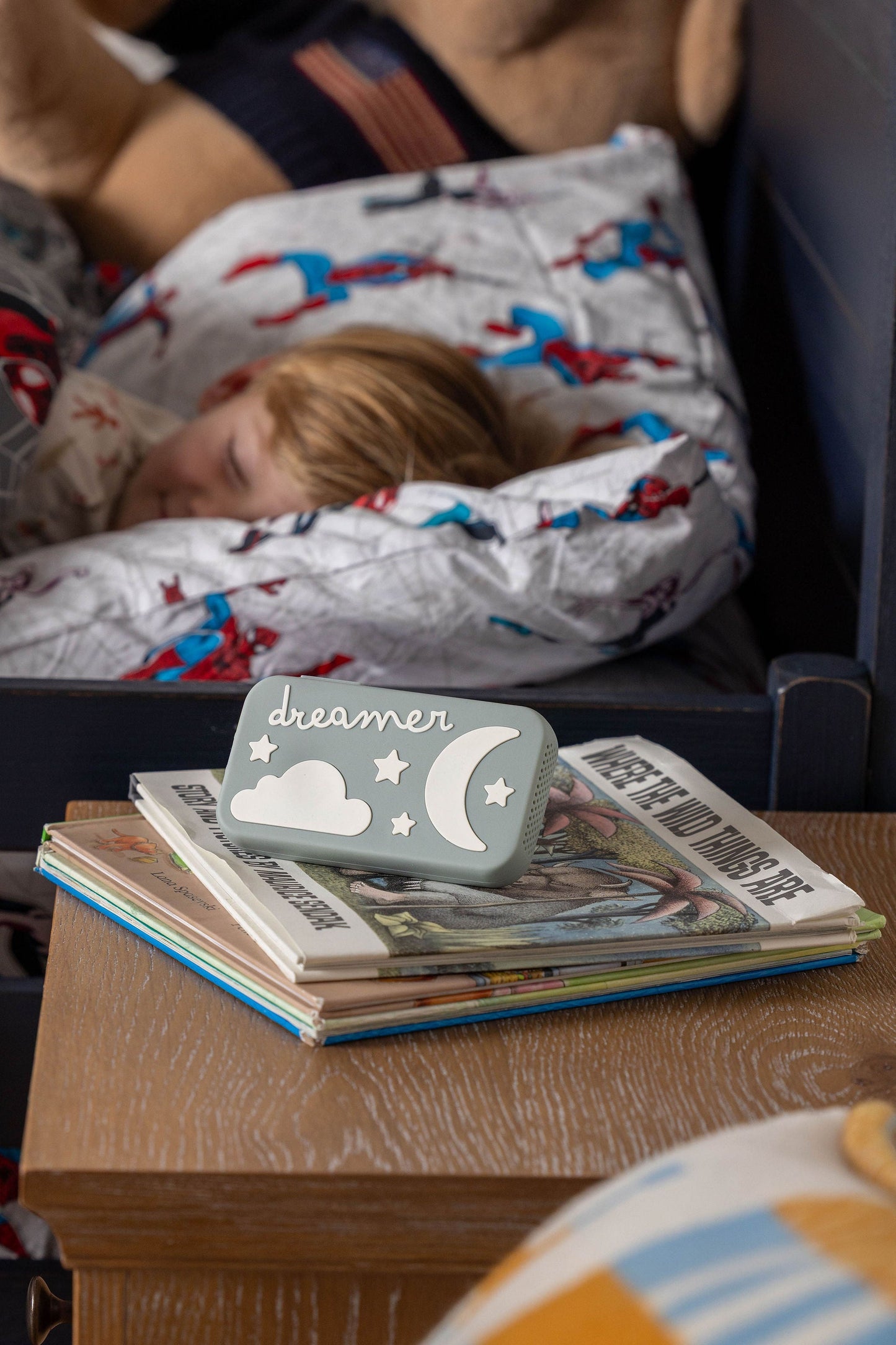 Child sleeping peacefully with a Dreamer™ baby sound machine from the Duo bundle on bedside books